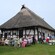 Guests dining outdoors near a historical building with a thatched roof